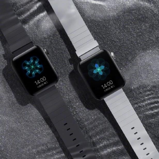 Zwei Xiaomi Smartwatches mit unterschiedlichen Armbändern liegen auf einer glitzernden Oberfläche.