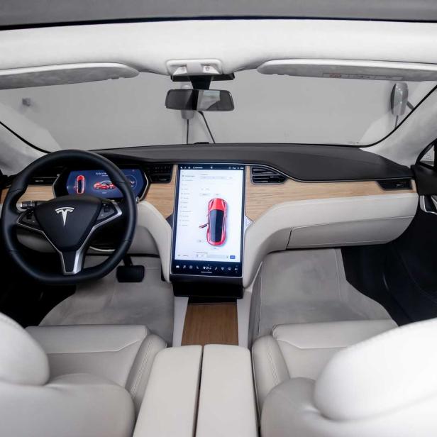Innenraum eines Tesla mit weißen Ledersitzen und einem großen Touchscreen-Display.