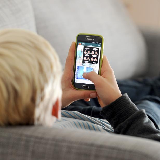 Symbolfoto: Ein Kind auf einer Couch spielt am Handy