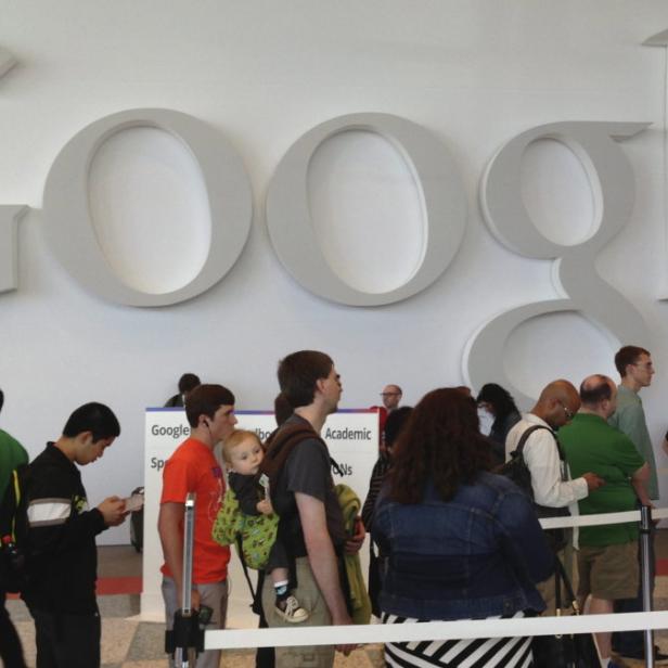 Menschen stehen vor einem großen Google-Logo an einer Wand Schlange.