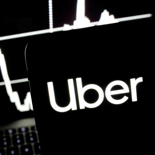 FILE PHOTO: Logo of the Uber is seen on a smartphone screen as a picture of stock exchange graph is displayed on a computer screen in this illustration picture