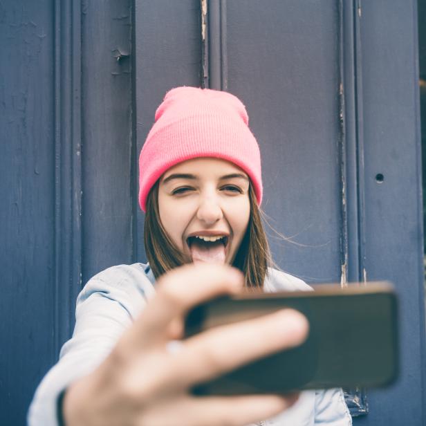 Ein Teenager-Mädchen macht ein Selfie und schneidet Grimassen.