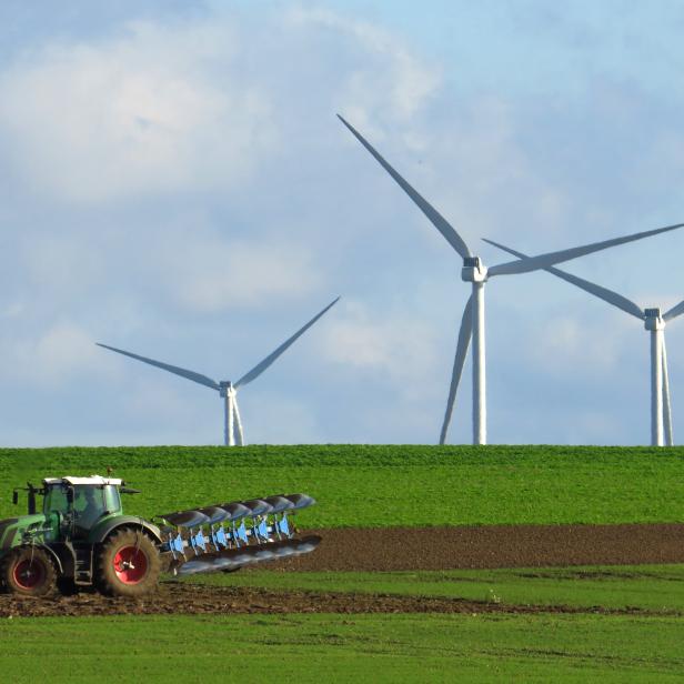 A French farmer drives a tractor as he ploughs a field in front of power-generating windmill turbines on a wind park in Havrincourt