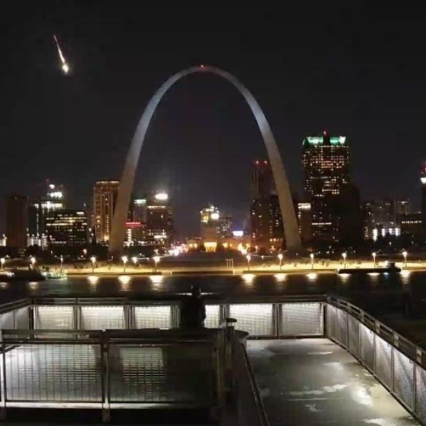 Der Gateway Arch und die Skyline von St. Louis bei Nacht mit einer Sternschnuppe am Himmel.