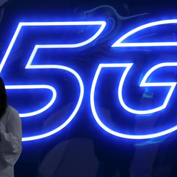 FILE PHOTO: A woman looks at her mobile phone next to a 5G sign at the Mobile World Congress in Barcelona