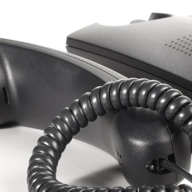 Ein schwarzes Tischtelefon mit Hörer und Spiralkabel auf einem Schreibtisch.