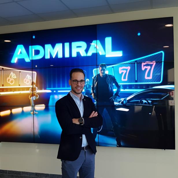 Ein Mann steht vor einer großen „Admiral“-Werbetafel mit Spielmotiven.