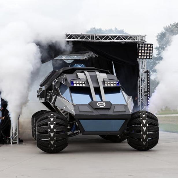 Ein futuristisches, schwarzes Geländefahrzeug steht vor einer Bühne mit Nebelmaschinen.