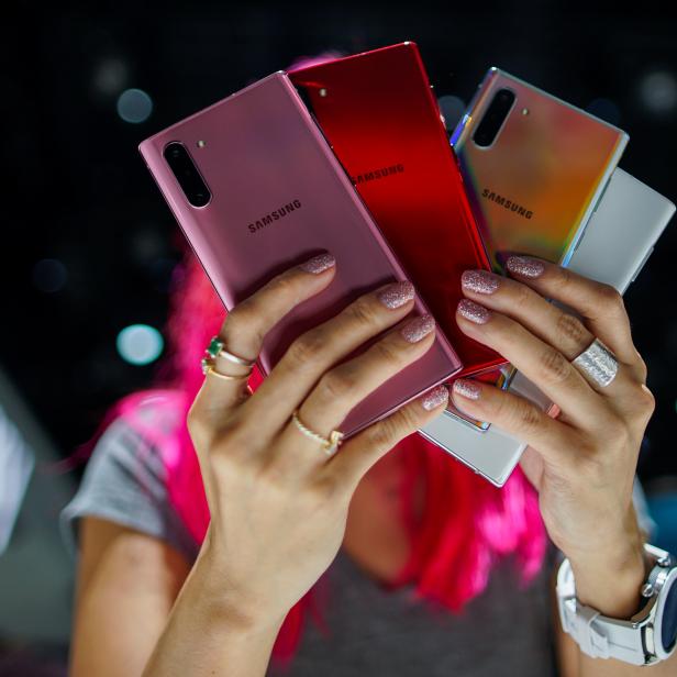 Eine Frau hält verschiedenfarbige Modelle des Samsung Galaxy Note 10, während Leute neue Geräte testen.