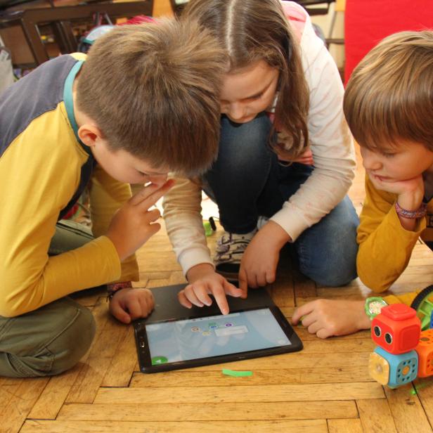 Drei Kinder vor einem Tablet auf dem Boden und einem selbst zusammengebauten Roboter