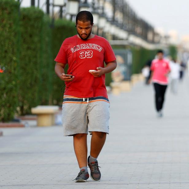 A Saudi man uses his smartphone as he walks on a sidewalk in Riyadh