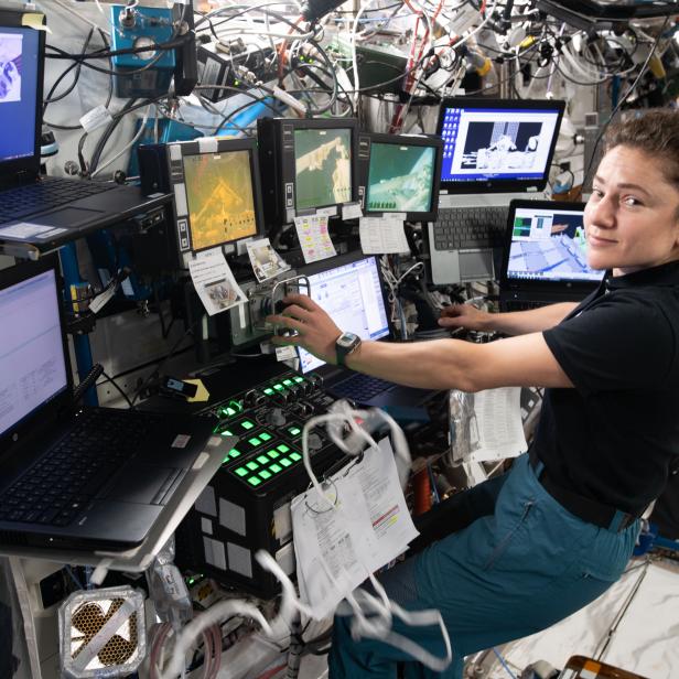 Eine Astronautin arbeitet in der Raumstation an mehreren Computern und Bildschirmen.