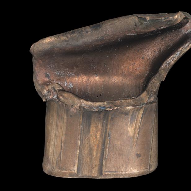 Ein beschädigtes, zylinderförmiges Objekt aus Metall vor schwarzem Hintergrund.