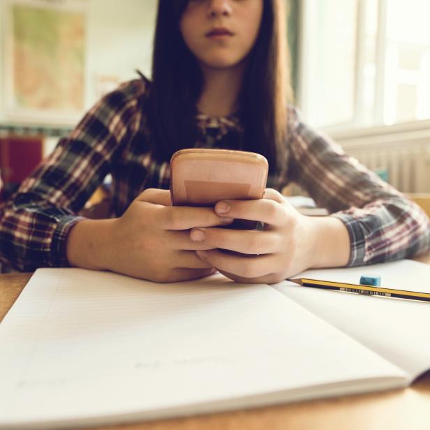 Close up of schoolgirl using mobile phone in the classroom.