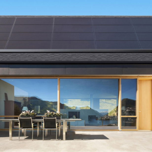 Ein modernes Haus mit Tesla-Solaranlage auf dem Dach und einem Tesla-Stromspeicher an der Wand.