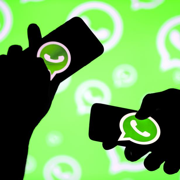 Männer posieren mit Smartphones vor dem angezeigten WhatsApp-Logo in dieser Illustration.
