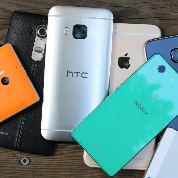 Mehrere Smartphones verschiedener Marken liegen auf einem Holztisch.