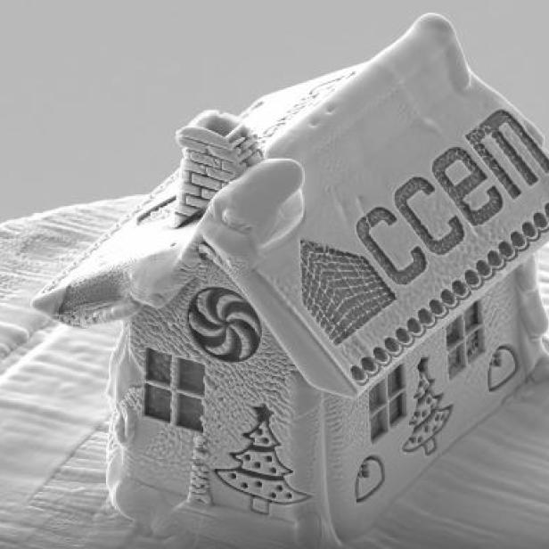 Ein winziges Lebkuchenhaus mit der Aufschrift „CCEM“ steht auf einer Oberfläche.