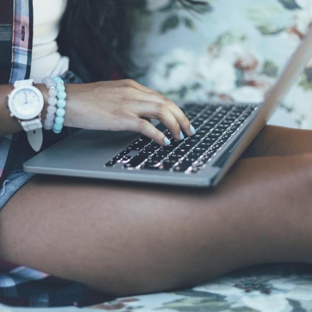 Eine Jugendliche sitzt mit einem Laptop auf dem Bett.