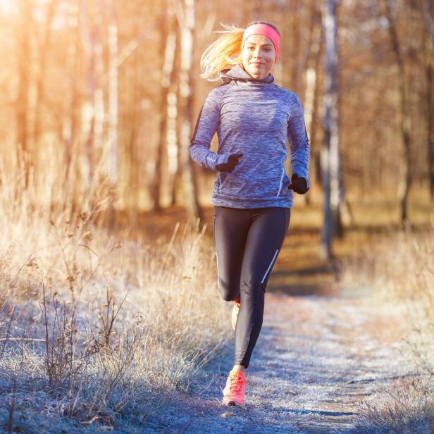 Eine Frau joggt an einem sonnigen Wintertag auf einem Weg.