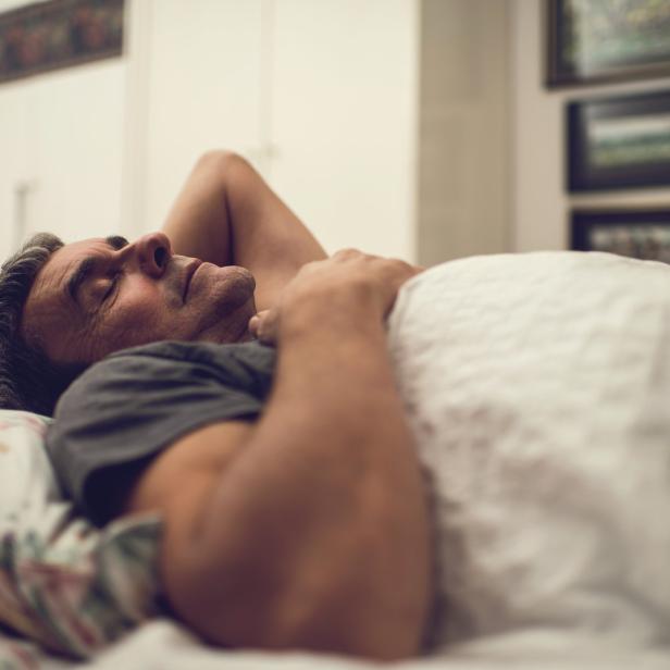 Ein Mann schläft in seinem Bett unter einer weißen Decke.