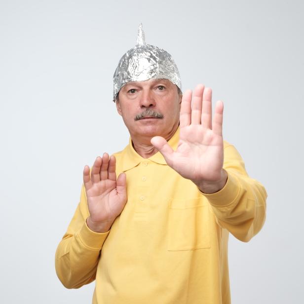 Caucasian mature man in a tin foil hat displeased closing his face with hands.