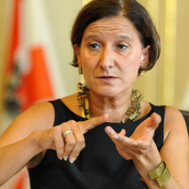 Eine Frau gestikuliert vor den Flaggen Österreichs und der Europäischen Union.