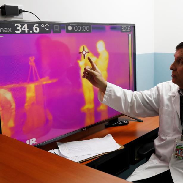 A doctor points to a monitor showing thermal scanners that detect temperatures of passengers at the security check inside the airport in Guatemala City