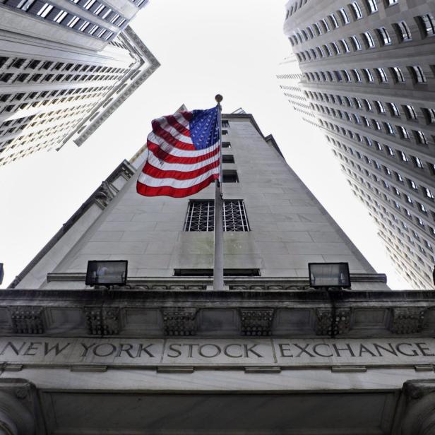 Die amerikanische Flagge weht vor der New York Stock Exchange zwischen hohen Gebäuden.