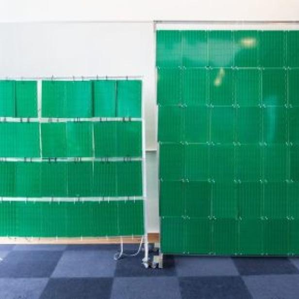 Zwei grüne, bewegliche Stellwände stehen in einem Raum mit blauem Teppichboden.