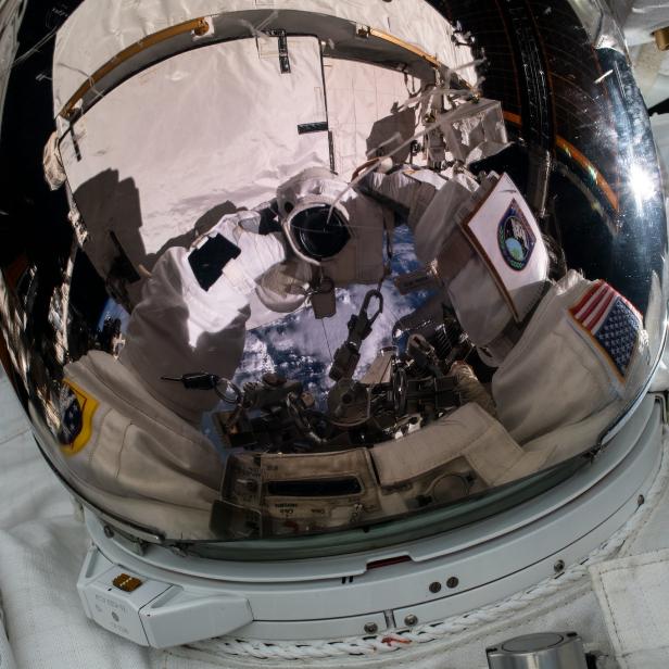Das Spiegelbild eines Astronautenvisiers zeigt die Internationale Raumstation und die Erde.
