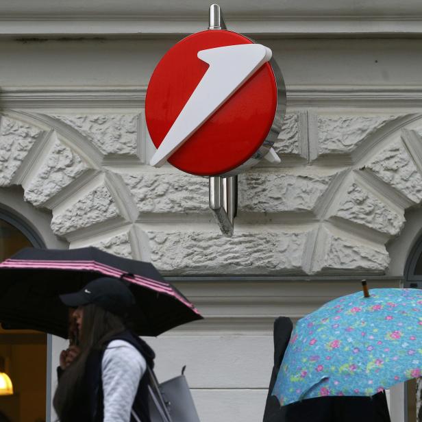 People carrying umbrellas pass a Bank Austria branch office in Vienna