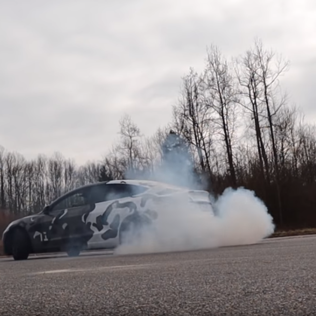 Ein Auto mit Tarnmuster macht auf einer Straße einen Burnout und erzeugt viel Rauch.
