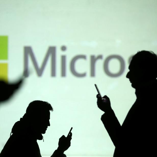 Silhouettes of mobile users are seen next to a screen projection of Microsoft logo in this picture illustration