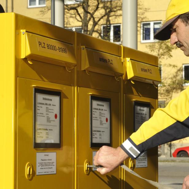 Ein Postbote der Deutschen Post öffnet einen gelben Briefkasten.