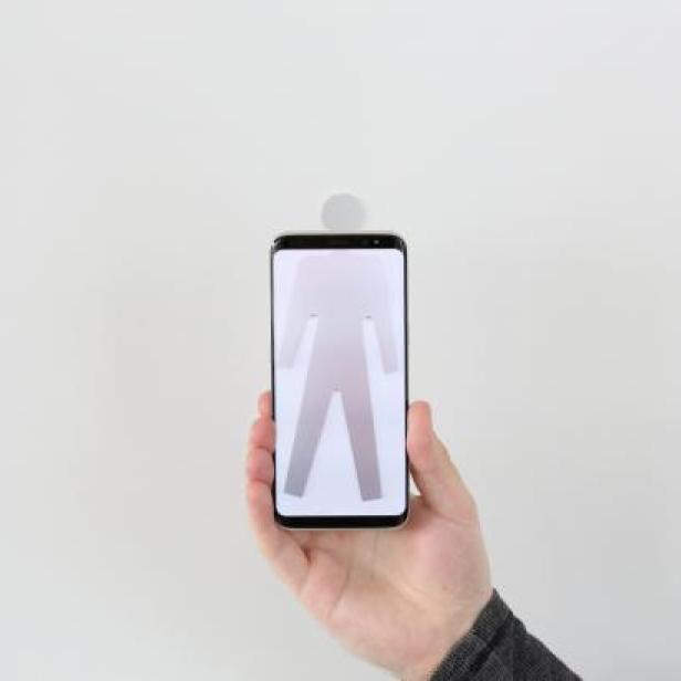 Eine Hand hält ein Smartphone, das ein Piktogramm einer Person anzeigt.