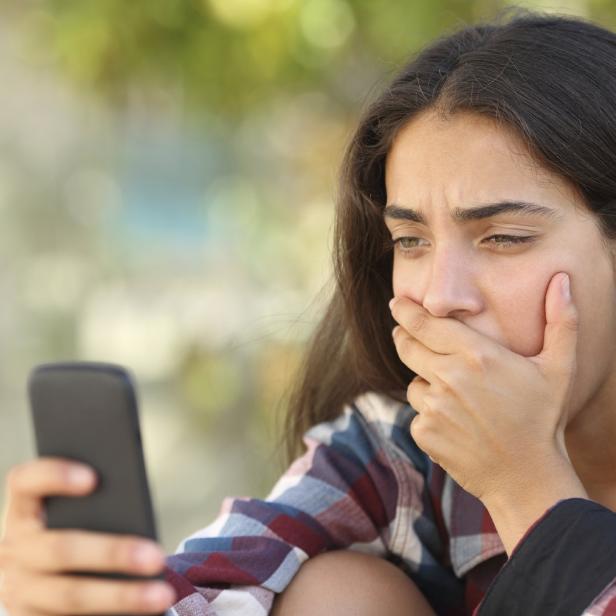 Eine Frau blickt verstört auf ihr Handy.