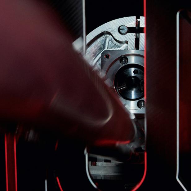Ein Finger berührt ein mechanisches Bauteil in einem dunklen Gehäuse.