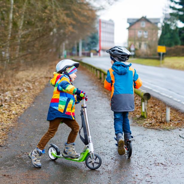 Two little kid boys, best friends riding on scooter in park