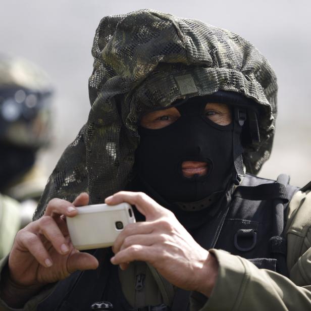 An Israeli soldier uses his mobile to take pictures during a protest against what Palestinians say is land confiscation for Jewish settlements, in Silwad