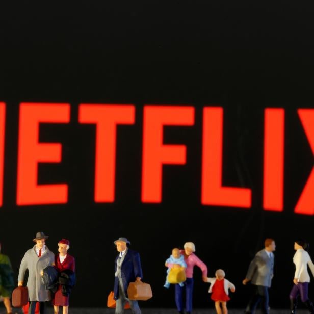Small toy figures are seen in front of diplayed Netflix logo
