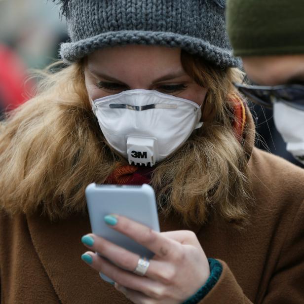 People wearing protective face masks use a smartphone on a street in Kiev