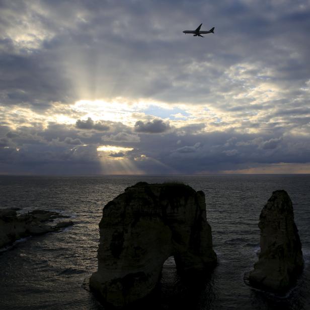 An airplane flies over the Pigeons' Rock as storm clouds loom during sunset in Beirut