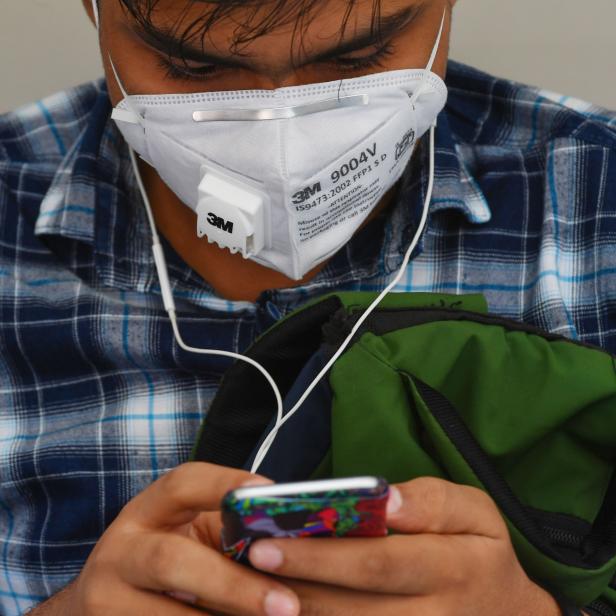 Ein Mann mit Atemschutzmaske und Kopfhörern blickt auf sein Smartphone.