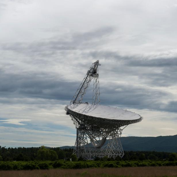 Ein großes Radioteleskop steht in einer ländlichen Gegend unter einem bewölkten Himmel.