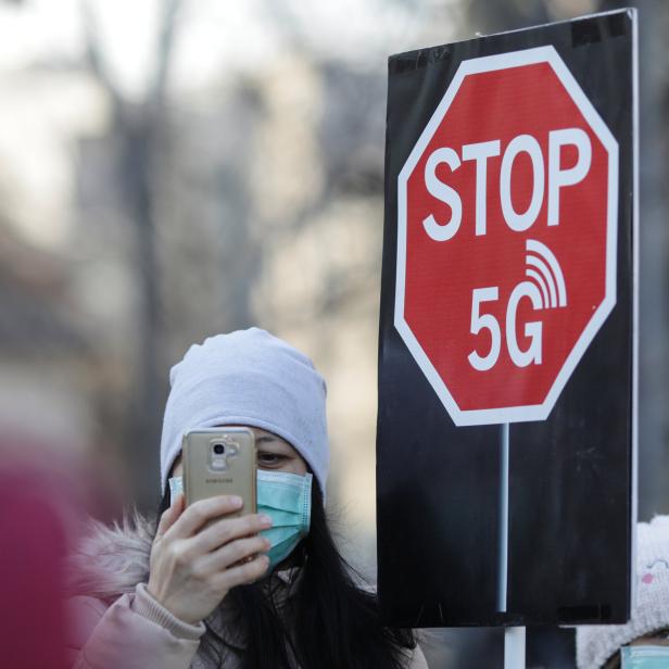 A woman uses her mobile phone while holding a placard reading " STOP 5G" during a protest against 5G technology
