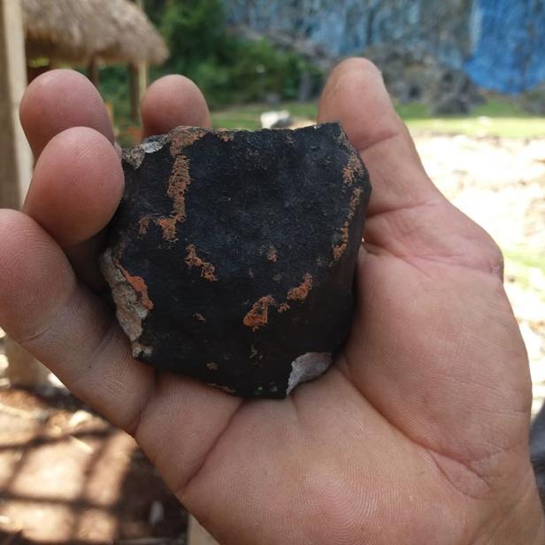 Eine Hand hält ein Stück eines schwarzen Meteoriten in Kuba.