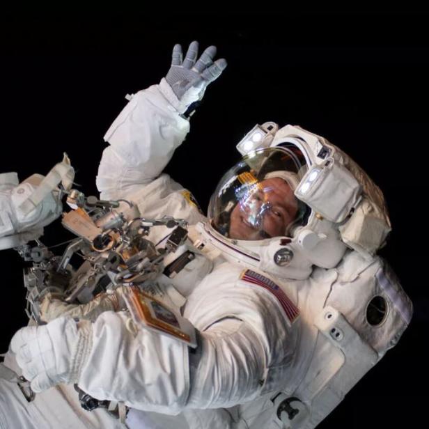 Ein Astronaut winkt im Weltraum, neben einer Raumstation.