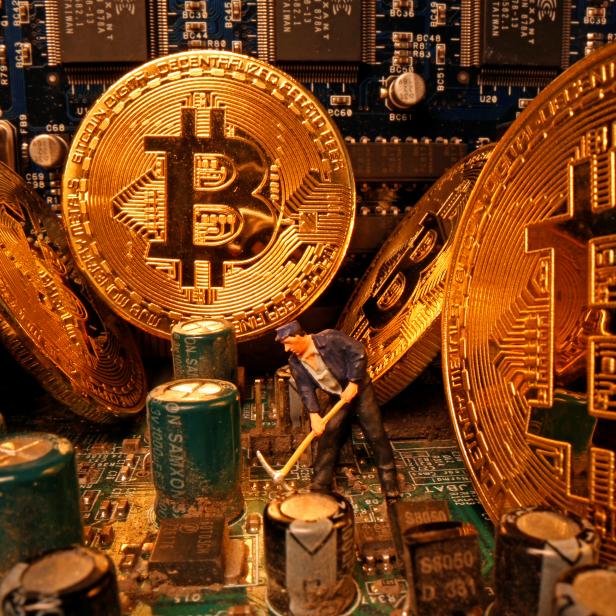 A small toy figure and representations of the virtual currency Bitcoin stand on a motherboard in this picture illustration