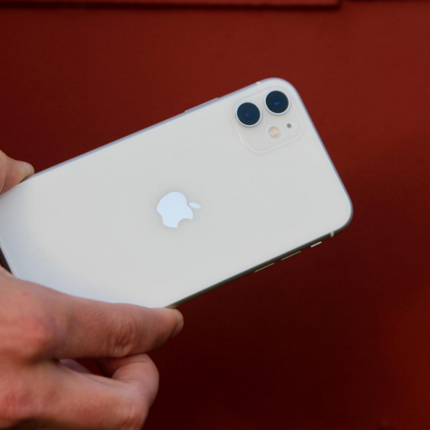 Eine Hand hält ein weißes iPhone vor einem roten Hintergrund.